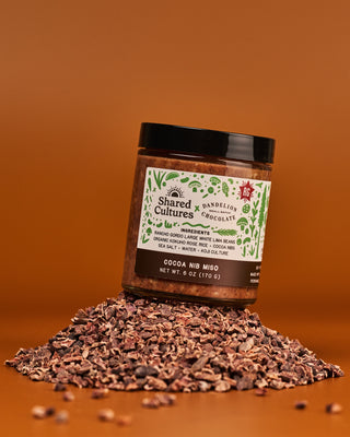 Jar of 'Shared Cultures' Cocoa Nib Miso sitting on a pile of cocoa nibs