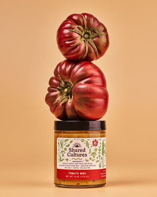 Jar of 'Shared Cultures' Tomato Miso with two heirloom tomatoes stacked on top of the jar