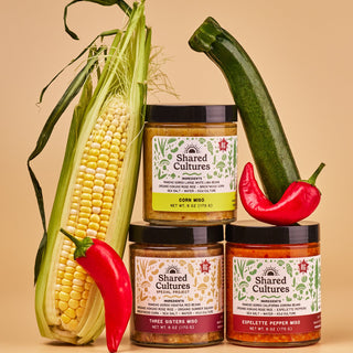 Three jars of 'Shared Cultures' miso with a corn cob, zucchini, and peppers