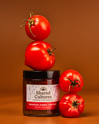 Jar of 'Shared Cultures' Preserved Summer Tomatoes with tomatoes stacked around the jar