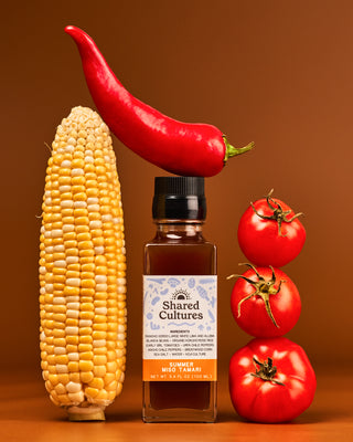One bottle of 'Shared Cultures' Summer Miso Tamari next to an ear of corn, three tomatoes and a pepper